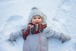 © kaloriya - Happy little toddler girl laying in snow and smiling.