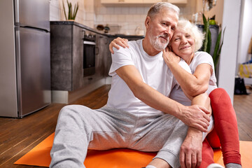 senior couple having rest on the floor after yoga exercises, in sportive wear, look at camera and smile