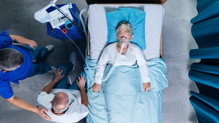 Wall Mural - Top view of doctors and covid-19 patient with oxygen mask in bed in hospital, coronavirus concept.