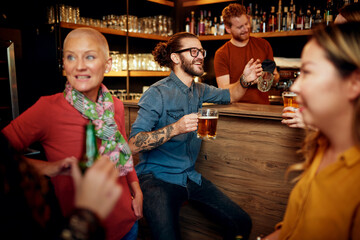 Wall Mural - Group of cheerful friends standing near bar counter, drinking beer and chatting.