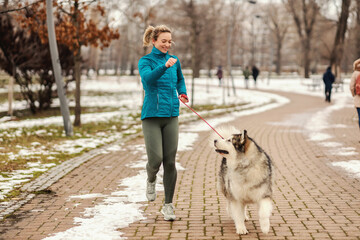 Woman playing with her dog while walking in park on snowy winter day. Pets, snow, friendship, weekend activities