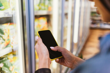 Close-up of a mobile phone in female hands on the background of a refrigerator