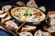 © Carey - Close up view of an artichoke dip surrounded by various breads and crackers for dipping.