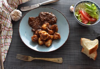 Croatian traditional cuisine, Pasticada With Gnocchi - Dalmatian Pot Roast or beef/ Croatian dish - Pasticada with gnocchi, beef stew in a sauce and served fresh salad at dark wooden background