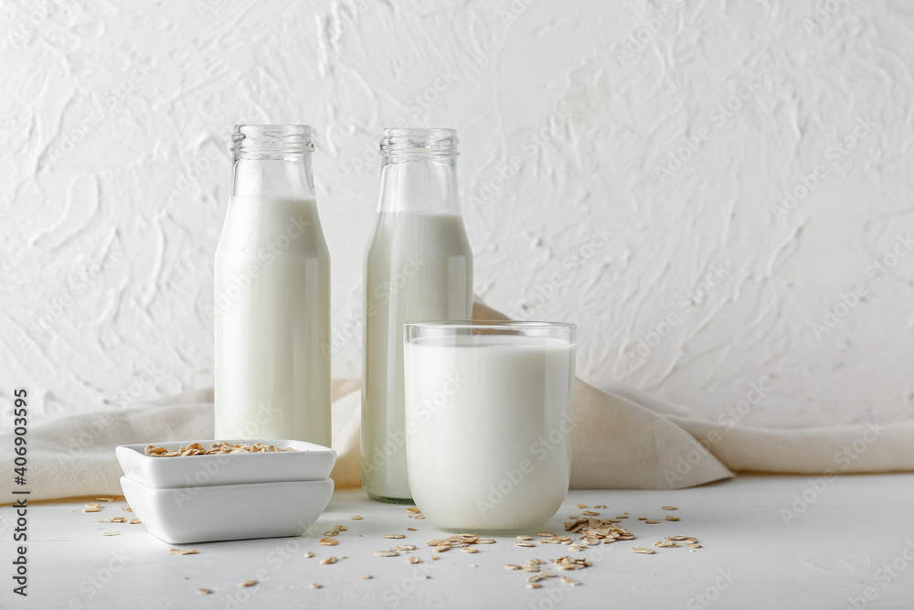 Bottles and glass of oat milk on light background