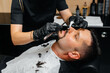 © Andrii - A professional stylist in a modern stylish barbershop shaves and cuts a young man's hair. Beauty salon, hair salon