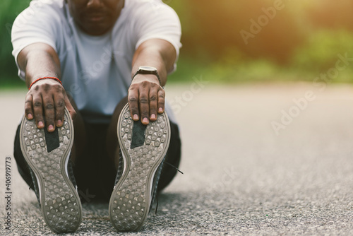 Close up Asian young athlete sport runner black man wear watch he sitting pull toe feet stretching legs and knee before running at outdoor street health park, healthy exercise before workout concept