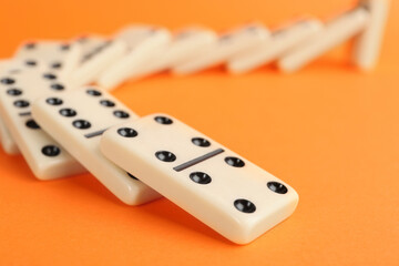 Wall Mural - White domino tiles falling on orange background, closeup