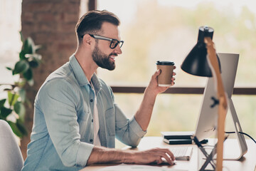 Poster - Photo portrait of guy holding coffee cup in hand working on pc at table in modern industrial office indoors