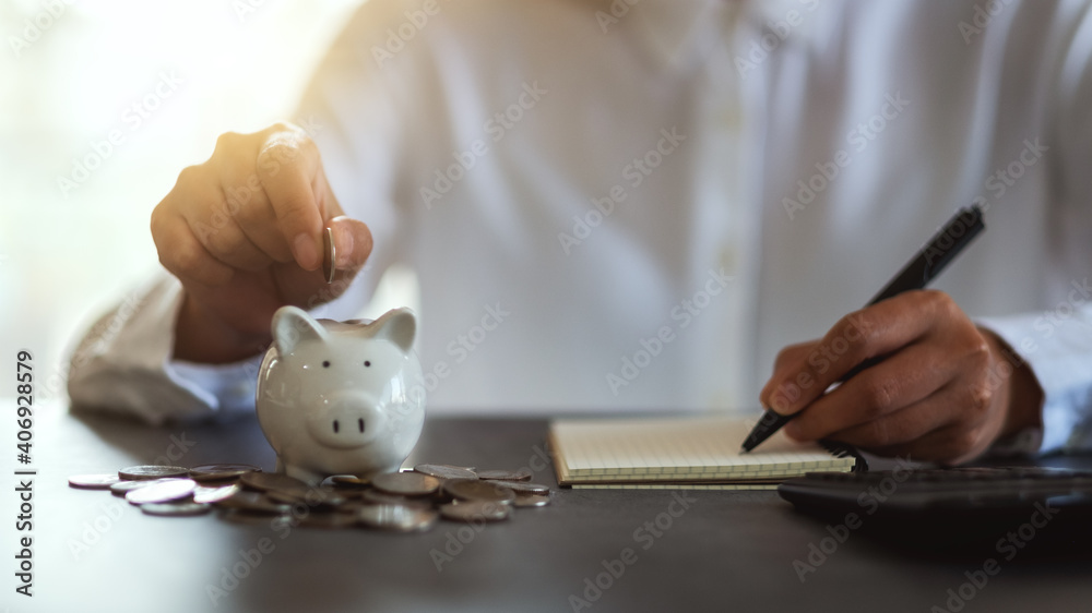 Closeup image of a woman putting coins in a piggy bank and taking note for saving money and financial concept
