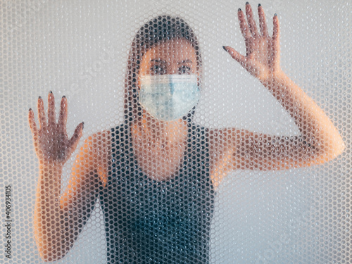 Air pollution. Defocused portrait. Ecology problem. Allergy gasp. Disturbed woman in protective face mask with breathing problem behind bubble wrap texture drop on neutral background out of focus.