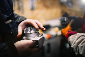 Automotive water pump of the engine cooling system in the hands of an auto mechanic, replacement of the pump with a metal impeller.