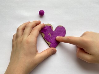 Children's hands smear pink plasticine on the heart. kids craft