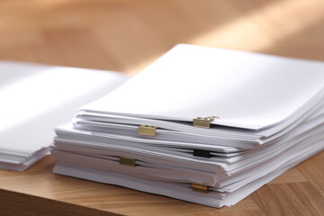 Stack of blank paper with binder clips on wooden table, closeup