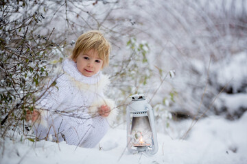 Canvas Print - Beautiful blond toddler child, boy with white knitted handmade overall, holding lantern in the snow