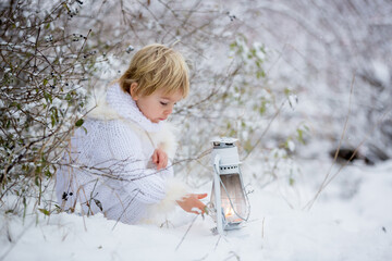 Wall Mural - Beautiful blond toddler child, boy with white knitted handmade overall, holding lantern in the snow