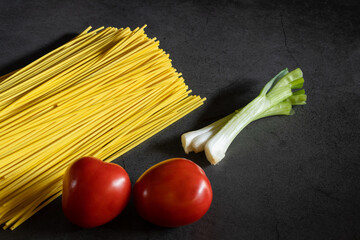 Yellow spaghetti and tomatoes on a black marble table. Yellow Italian Pasta. Raw spaghetti. Italian concept and menu