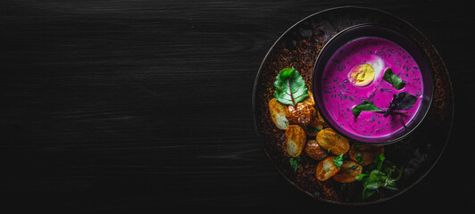 Wall Mural - Cold beetroot soup with sour cream, egg and hot potatoes in bowl on black wooden table background