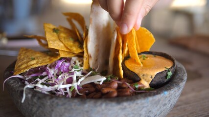 Hand dipping nacho in vegan creamy sous. Healthy vegan Mexican bowl with salsa, beans and dips