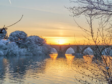 People Walking On A Stone Bridge At Sunset And The Frozen Trees In Winter At The Golden Hour