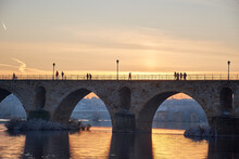 People Walking On A Stone Bridge At Sunset And The Frozen Trees In Winter At The Golden Hour