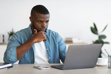 focused african american businessman working with laptop at office