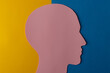Head silhouette made of paper. Pink paper shaped as a human head with copy space on yellow and blue paper background.
