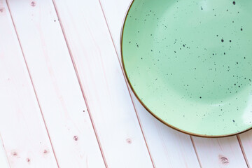 Light green ceramic plate with  on white wooden background. Top view