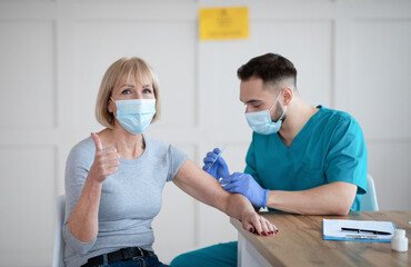 Poster - Senior female patient recommending covid-19 vaccination, gesturing thumb up during coronavirus vaccine injection