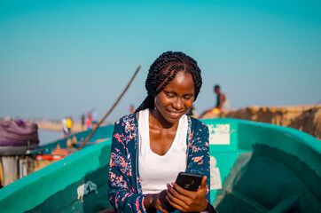 beautiful young african lady sitting by the river side feeling excited as she operate her cellphone