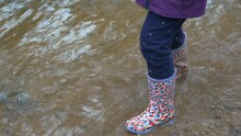 Young Child Walking And Splashing Water In Welly Boots