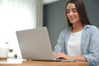 © New Africa - Young woman using laptop for search at wooden table in room
