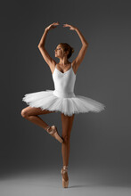 Graceful Ballerina In White Tutu And Pointe Shoes On Gray Background