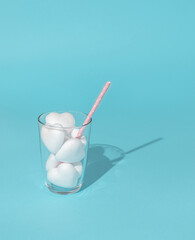 Glas of white hearts with bright pink paper straw on pastel blue background. Minimal concept.