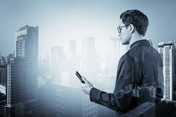 Young handsome businessman in suit and glasses using phone and thinking how to tackle the problem, new career opportunities, MBA. Bangkok on background. Double exposure.