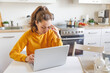 Mobile Office at home. Exhausted tired woman working using on laptop holding head in hand sitting in kitchen at home. Young girl studying or working indoors. Freelance business quarantine concept.