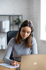 Beautiful young girl studying online using laptop web camera, writing lecture in notebook.Online education, remote working, home education.Online meeting,video call, video conference, courses online.