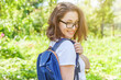 Happy beautiful positive student girl in eyeglasses with backpack smiling on green park background. Woman having rest in campus during lunch break. Education and leisure concept.