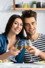 cheerful couple toasting glasses of wine in kitchen