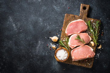Wall Mural - Pork meat. Fresh pork steaks on cutting board with ingredients for cooking. Top view at black stone table.