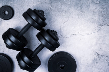 Top view of black dumbbells and different weight plates on gray textured background. Flat lay. Fitness or bodybuilding sport training concept. Copy space.