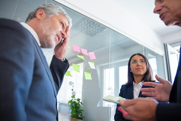 Wall Mural - Business colleagues discussing work issues, planning project together, talking at sticky notes on glass wall. Teamwork or management concept