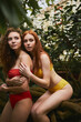 © Roman - two slender women in bikini posing on tropical tree trunk in forest, hugging each other. models in colourful swimwear in wild nature