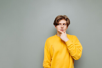 Wall Mural - Pensive guy in casual clothes stands against a gray wall and looks away with reflections on copy space. Isolated.