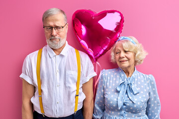 sad man and happy mature woman with ait ballon, celebrating saint valentines day isolated on pink background