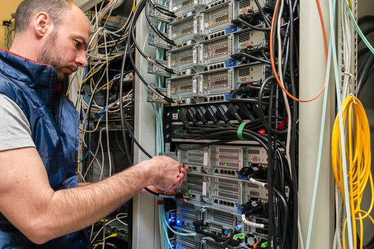 The man serves the server hardware. A technician switches internet wires in a server room. The specialist works with computer equipment in the data center