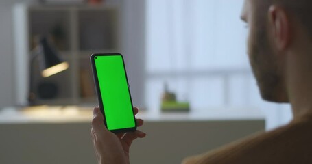 man is holding modern smartphone with green screen for chroma key technology, viewing video in social nets