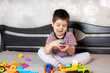© Zarina Lukash - A 3-4-year-old boy is playing on the bed with colorful construction blocks. Kindergarten children's educational games. For a toy store, day care center or nursery school