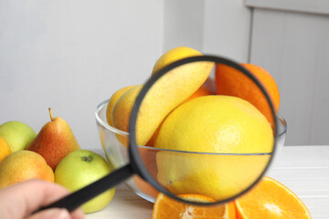Wall Mural - woman with magnifying glass exploring lemons indoors, closeup. poison detection