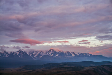 Wall Mural - scenic mountain landscape with great snowy mountain peak lit by orange dawn sun among low clouds. aw
